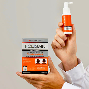 双手拿着FOLIGAIN男士10% TRIOXIDIL外用护理产品的包装盒和喷雾瓶。